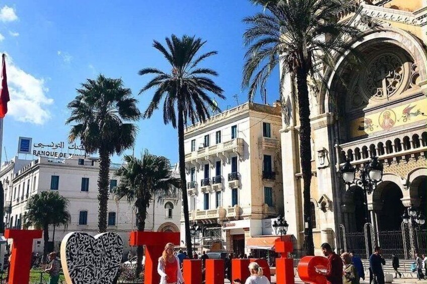 A historic building with ornate architecture, palm trees, and a red sculpture. 1