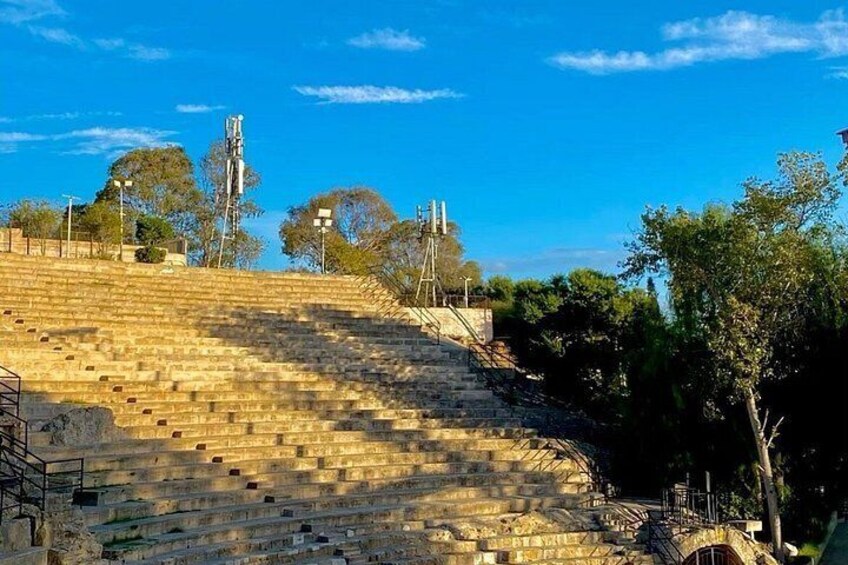A stone amphitheater with tiered seating, surrounded by trees and under a clear sky. 4
