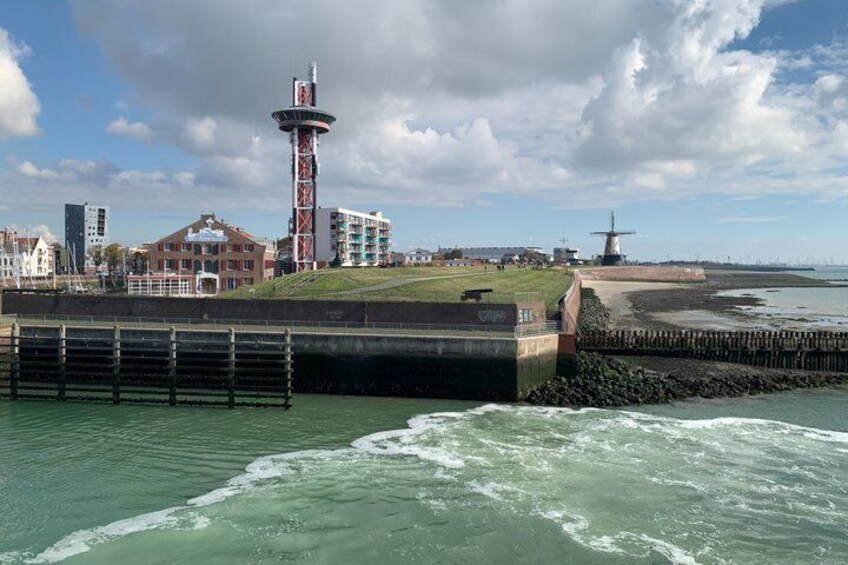 A coastal cityscape with a lighthouse, a windmill, and a sea wall. 1