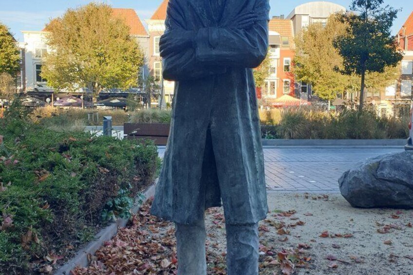 A statue of a person in a park with buildings in the background. 5