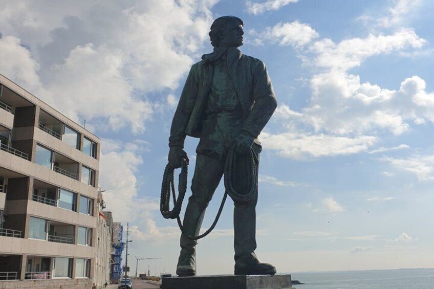 A statue of a man in uniform holding a rifle and a rope, standing on a platform with a modern building in the background. 2