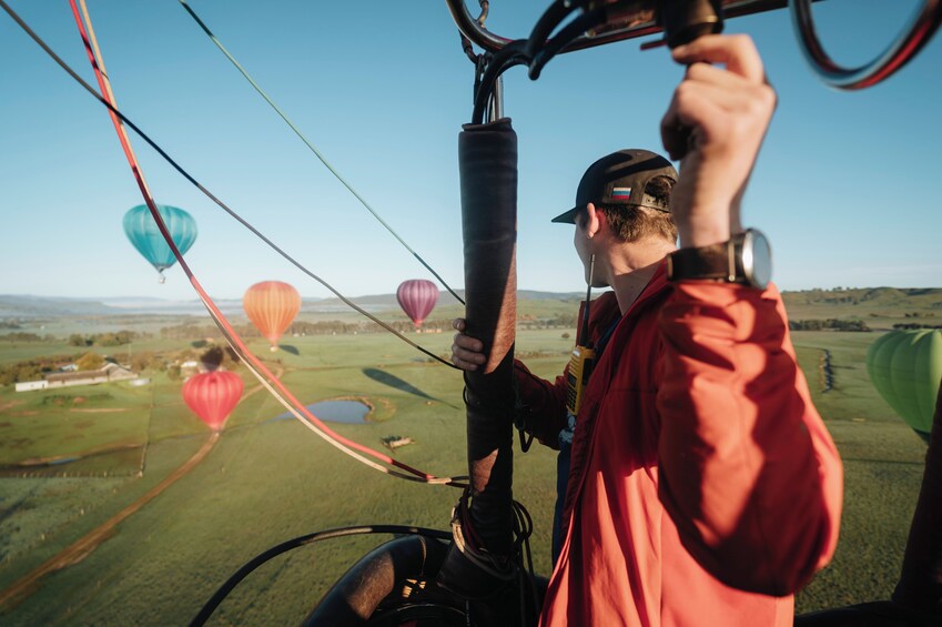 A person in a red jacket operating a hot air balloon with multiple colorful balloons in the background. 4