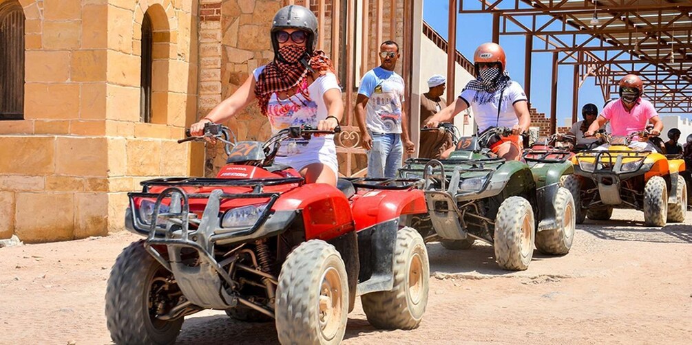 A group of people on ATVs lined up in front of a building with stone walls. 3