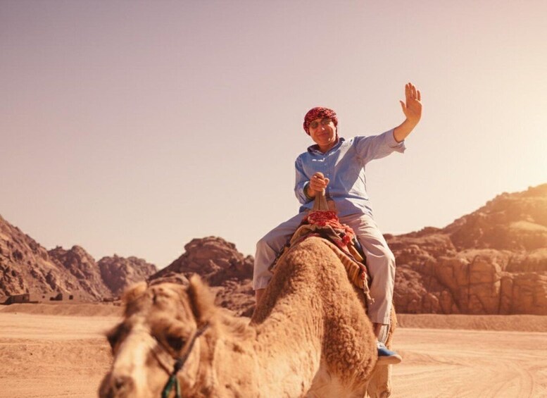 A person riding a camel in a desert landscape with rocky terrain and a clear sky. 4