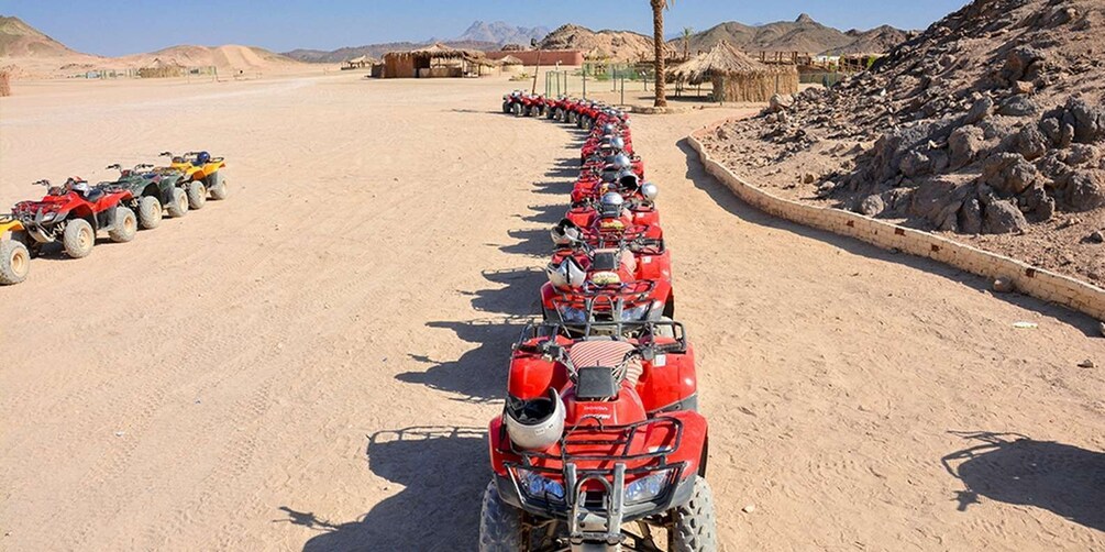 A row of ATVs parked on a dirt road in a desert landscape with mountains in the background. 5