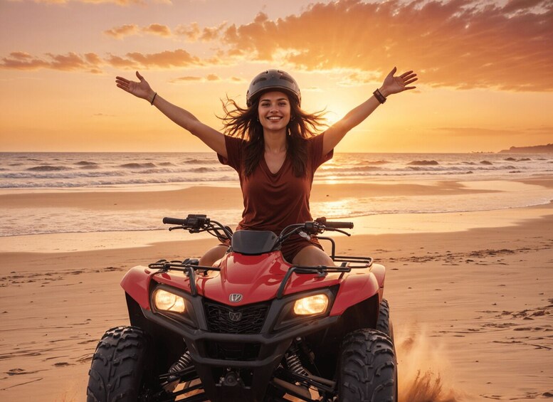 A person on a red ATV on a beach with arms raised, facing the ocean at sunset. 1