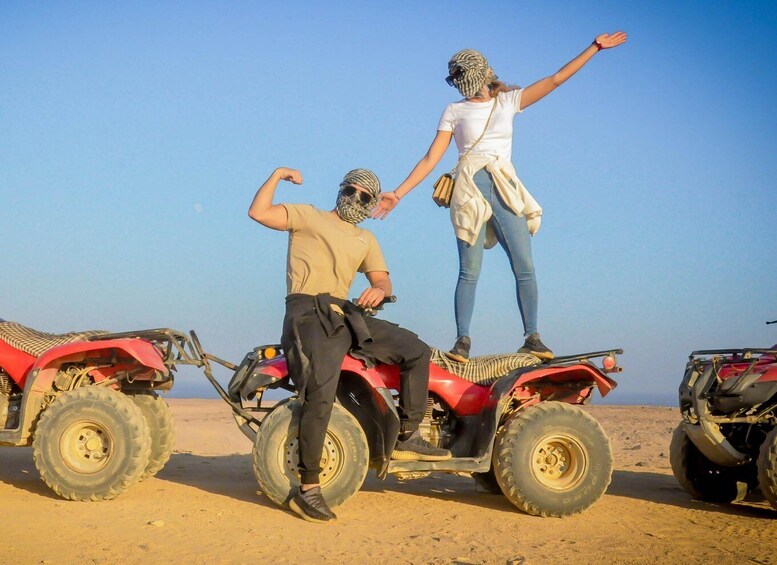 Two people on a red ATV in a desert with clear skies. 3