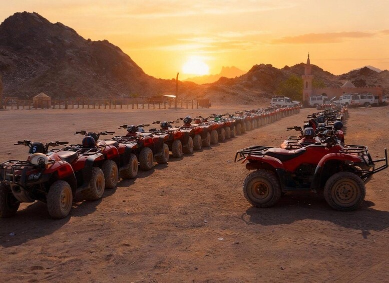 A row of red ATVs parked on a dirt road with a sunset in the background. 5