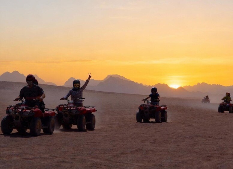 Four people riding quad bikes in a desert landscape during sunset. 3