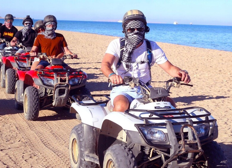 A group of people riding ATVs on a sandy beach with the ocean in the background. 1