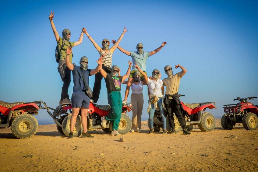 A group of people posing with raised arms in a desert landscape with ATVs in the background. 5