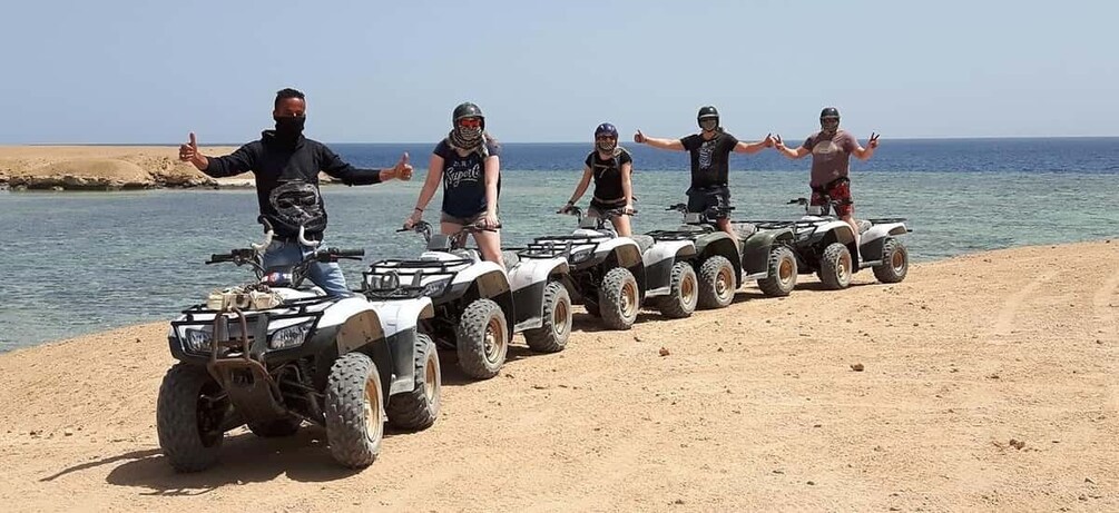 A group of people on ATVs lined up on a beach with the sea in the background. 2