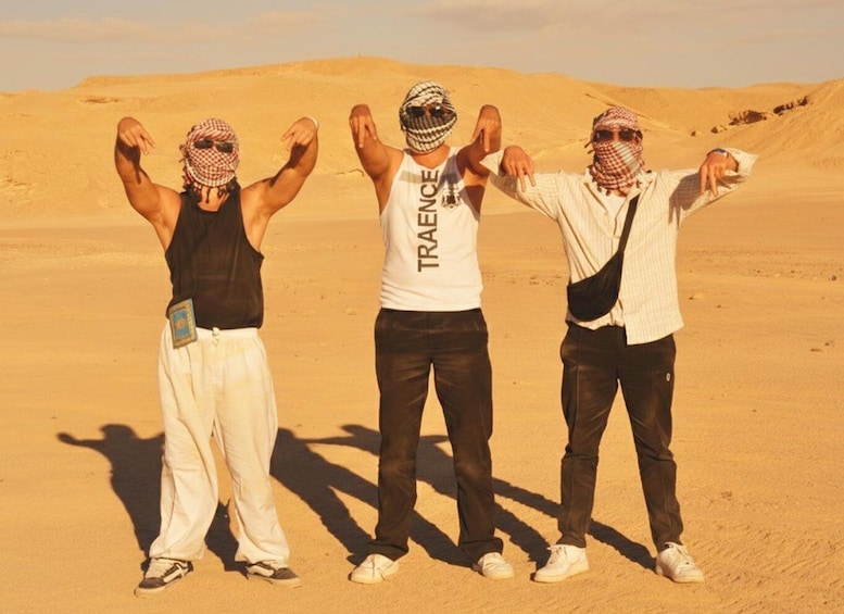 Three people standing in a desert with sand dunes in the background. 2