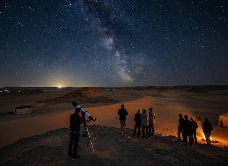 A desert landscape at night with a starry sky, a telescope, and people observing the stars. 5