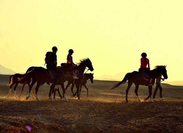 A group of people riding horses across a barren landscape during sunset. 4