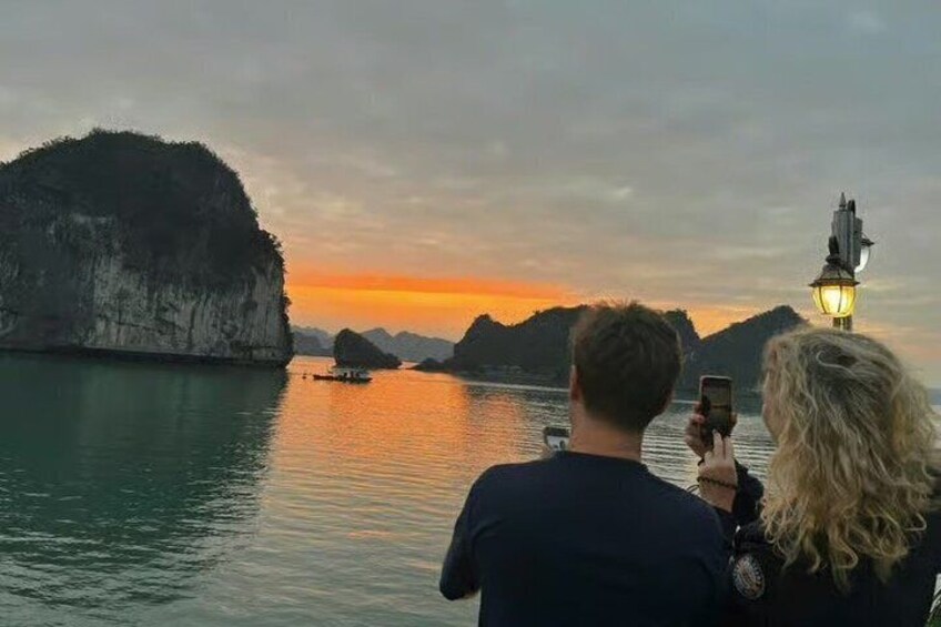 A couple taking a photo of a sunset over a body of water with a boat and a distant island. 5