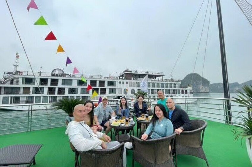 A group of people dining on a boat with a large ship in the background. 2