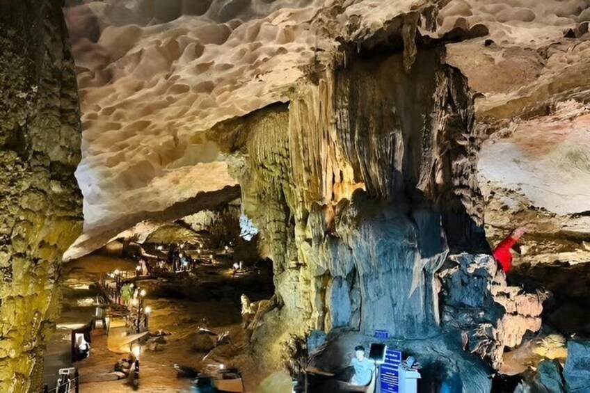 A cave with stalactites and stalagmites, illuminated by artificial lighting, with people exploring and a guide leading a tour. 3