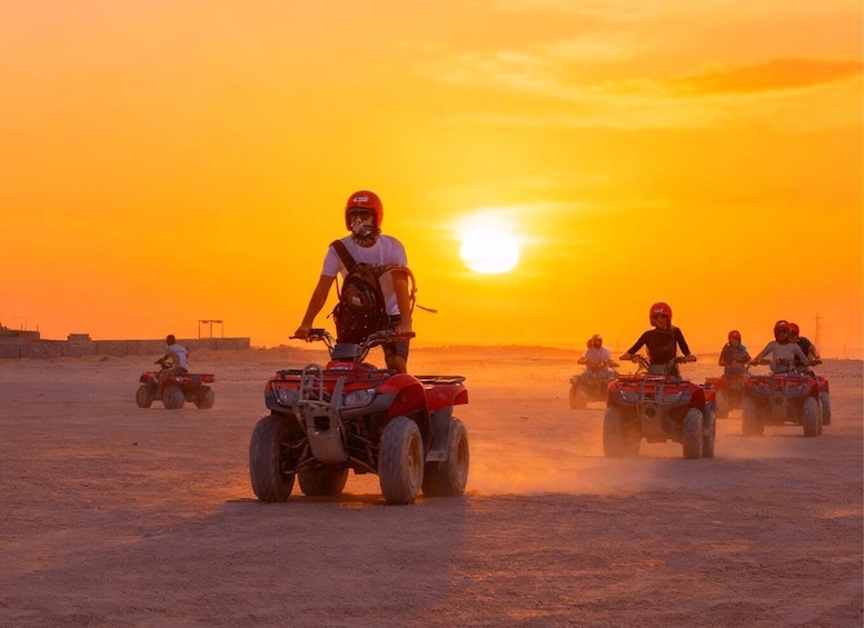 A group of people riding quad bikes in a desert at sunset. 1