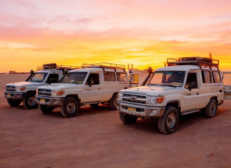 Three white off-road vehicles parked on a sandy beach at sunset. 2