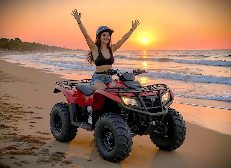 A person on a red ATV on a beach at sunset. 5