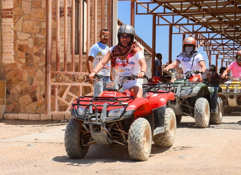 People riding ATVs on a dirt path with a stone wall and metal gate in the background. 4
