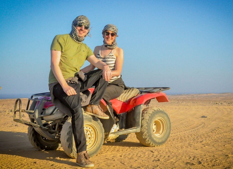 Two people on a red quad bike in a desert. 3