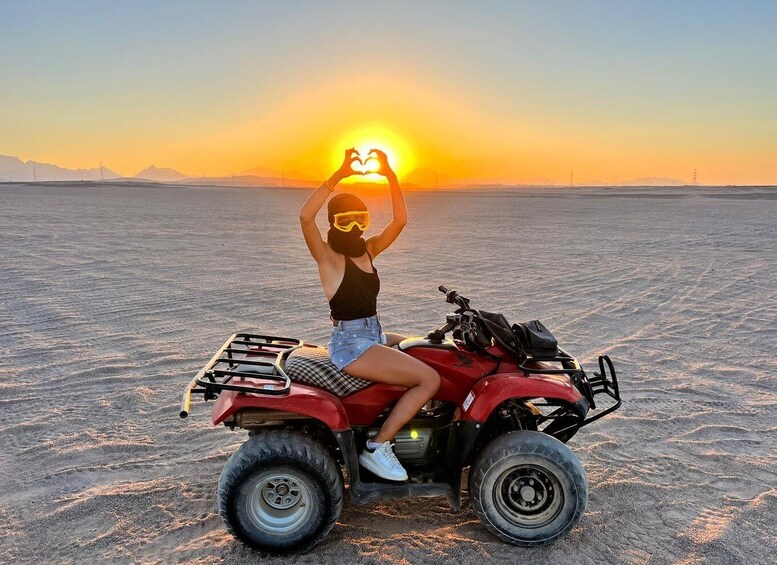 A person on a red ATV in a desert with the sun setting in the background. 1