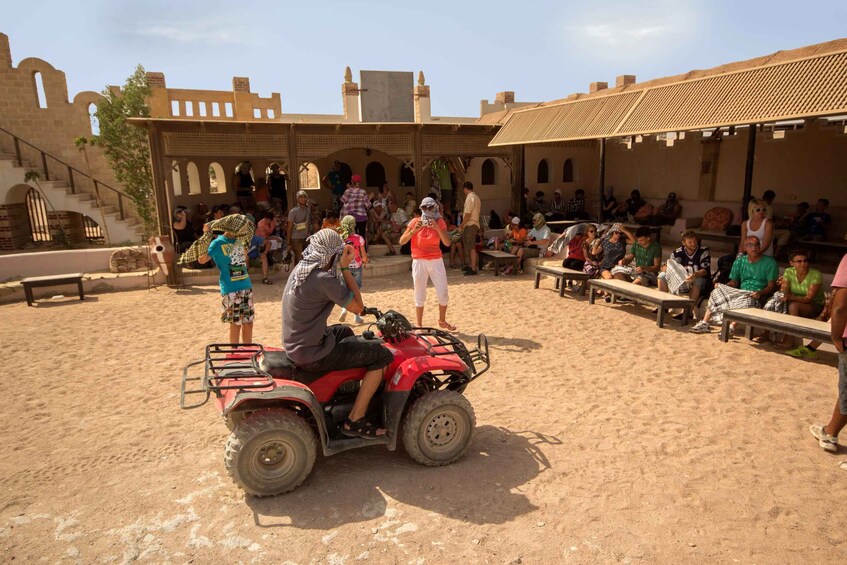 A sandy outdoor area with people, a red ATV, and traditional architecture. 4