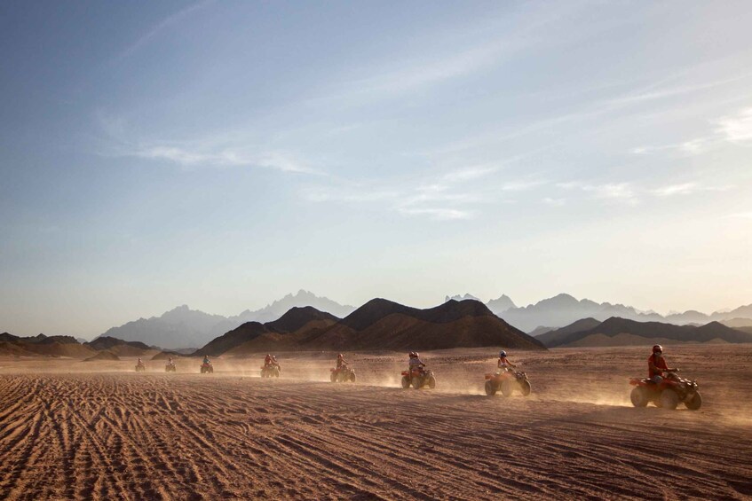 A group of people riding quad bikes on a sandy terrain with mountains in the background. 5