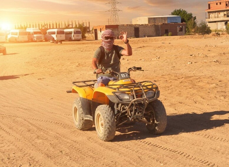 A person on a yellow ATV in a desert with buildings and power lines in the background. 3