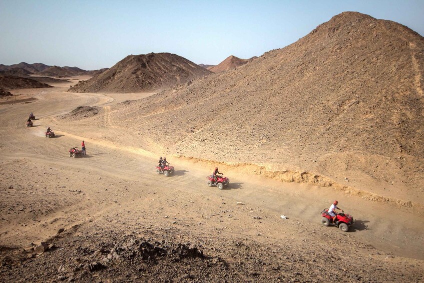 A group of people riding quad bikes on a dirt track in a desert landscape. 2