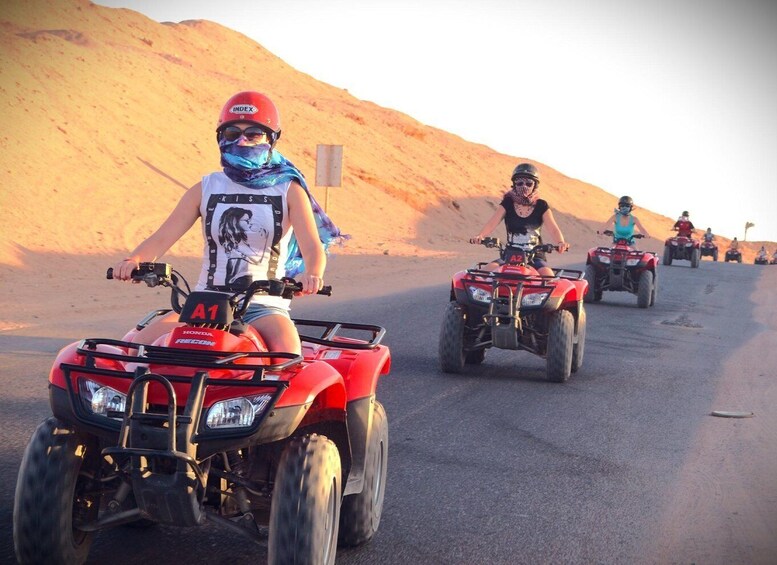 People riding ATVs on a road with desert hills in the background. 1