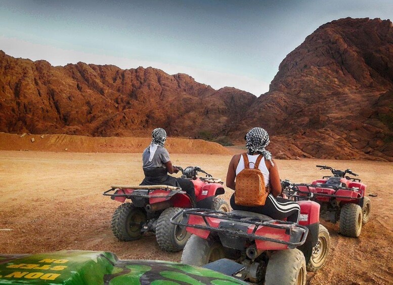 Two people on ATVs in a desert with rocky mountains in the background. 5
