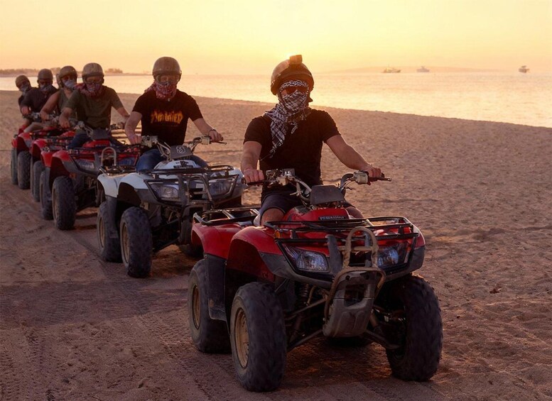 A group of people riding ATVs on a beach at sunset. 3