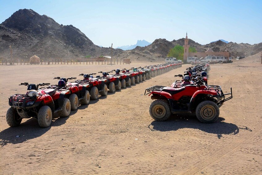 A convoy of red ATVs lined up on a dirt road with mountains in the background. 4