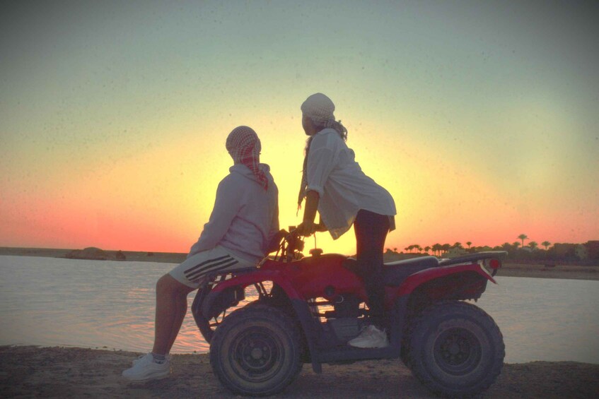 Two people on an ATV by a body of water during sunset. 1