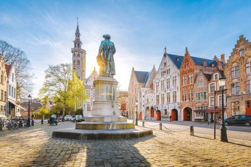 A cobblestone square with a statue, historic buildings, and a church tower. 3