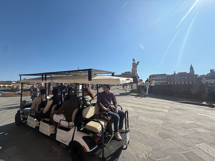 A golf cart with passengers, a statue, and buildings in the background. 2