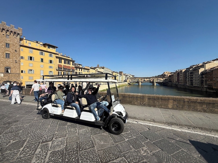 A group of people on a golf cart along a river with historic buildings in the background. 3