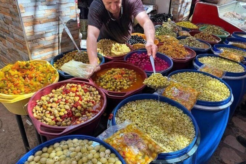 A vendor selecting olives from a large bowl at a market stall. 5