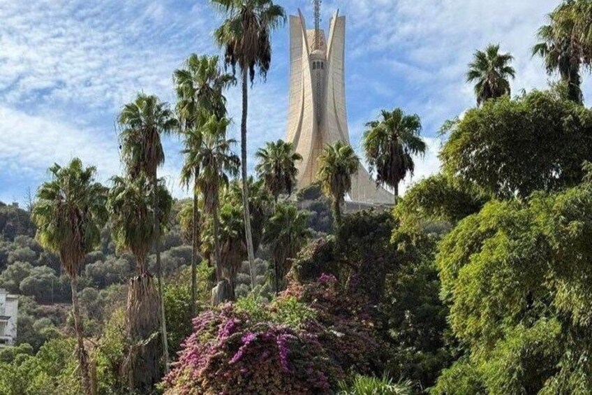 A modern building with a unique design, surrounded by lush greenery and palm trees. 1