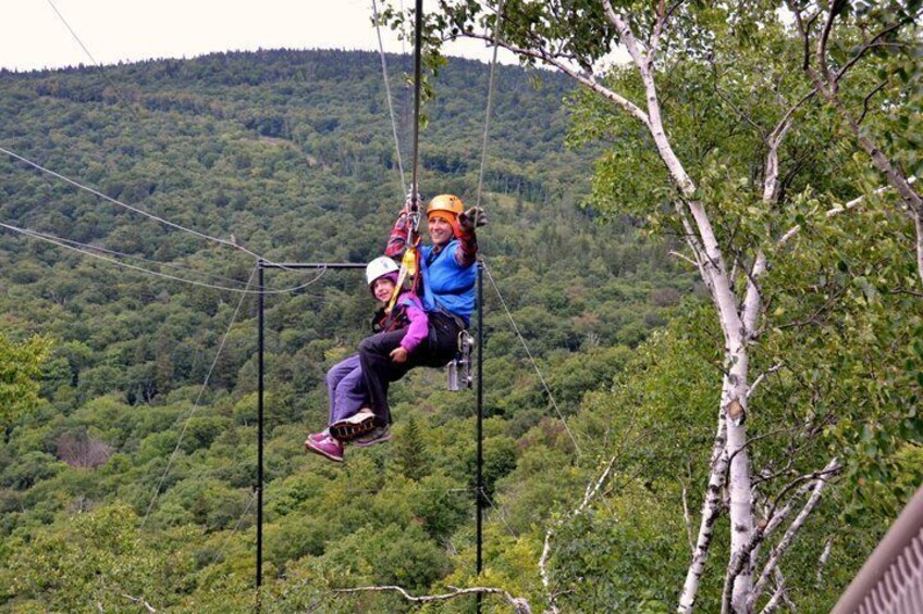 Two people on a zip line over a forested area. 2