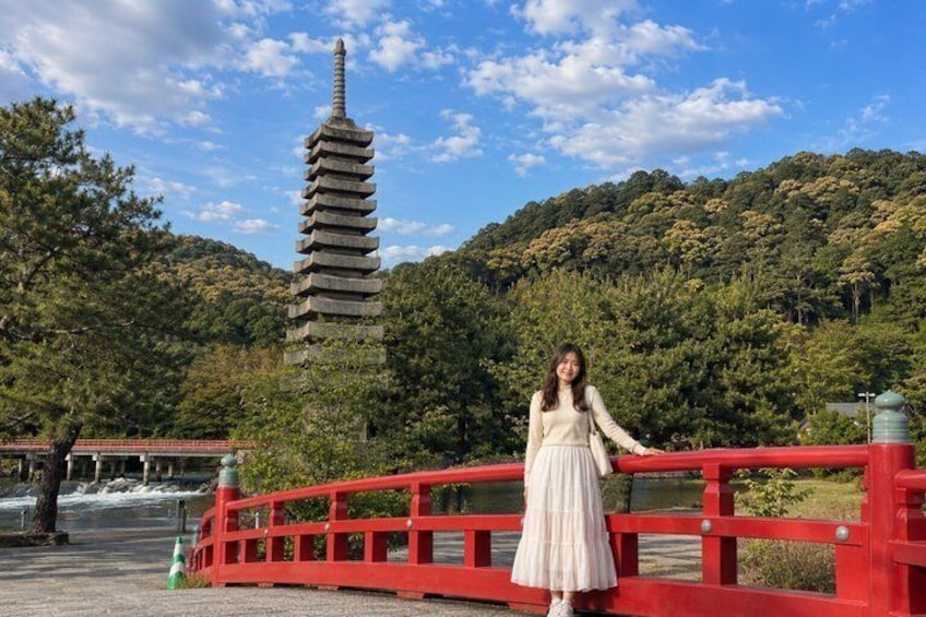 A person standing on a red bridge with a pagoda in the background. 5