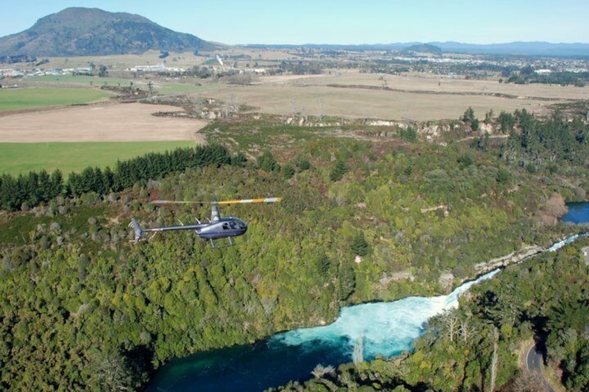 A helicopter flying over a river surrounded by dense forest and mountains. 1