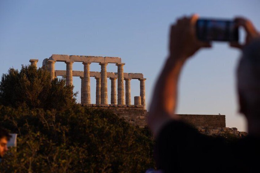 Ancient ruins with columns, a person taking a photo, and some foliage in the foreground. 4