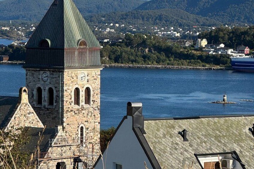 A stone tower with a clock, a body of water, and a distant town. 5