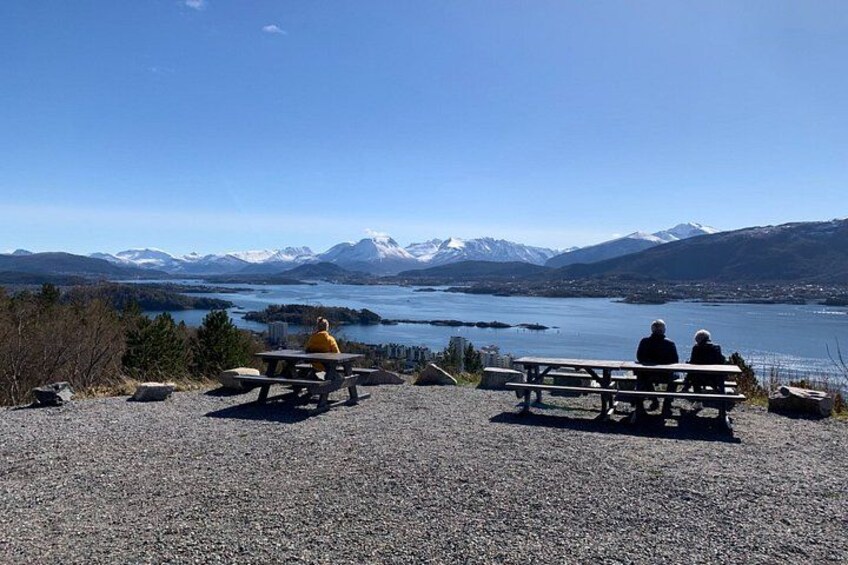 Two people sitting on benches overlooking a lake with mountains in the background. 1