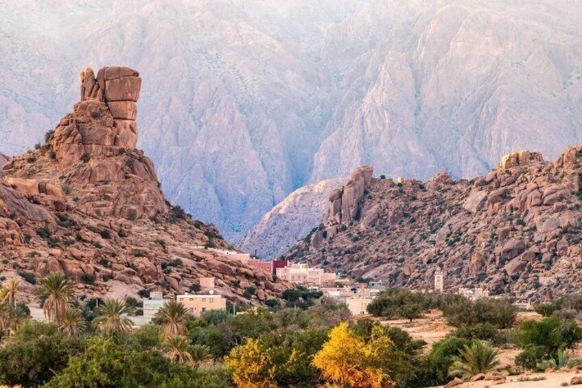 A rocky canyon with a prominent rock formation, a small settlement with buildings, and sparse vegetation. 1