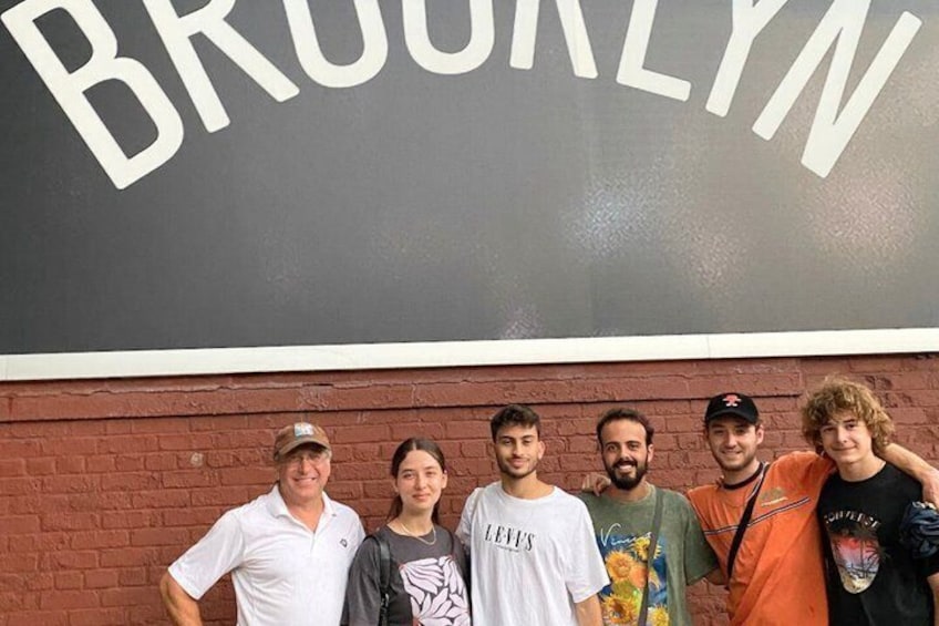A group of people standing in front of a wall with the word 'BROOKLYN' painted on it. 1